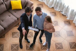 Realtor with house plan showing young couple around property for sale, above view